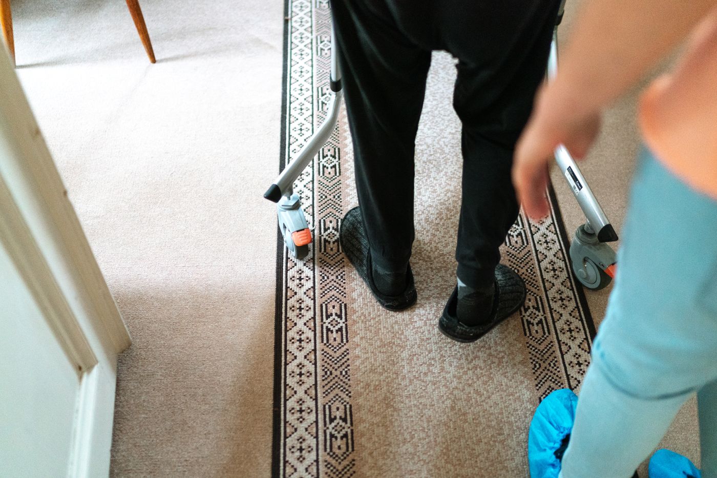 Home health therapist supporting an older adult walking with a walker inside the home